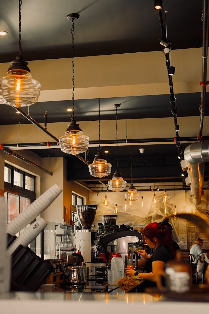 Warm cafe interior with industrial lighting and barista at work, creating inviting ambiance.